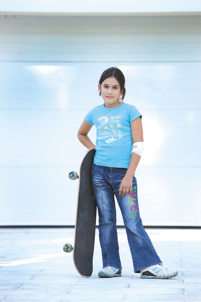 Girl (8-9) standing with skateboard in front of garage door, portrait